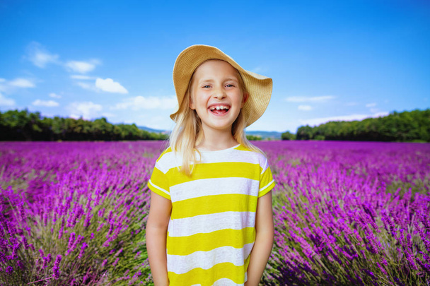 Portrait of smiling child in yellow t-shirt and straw hat in lavender field in Provence, France. Gorgeous view on Valensole plateau with blooming lavender field around the last week of June. - Фото, изображение