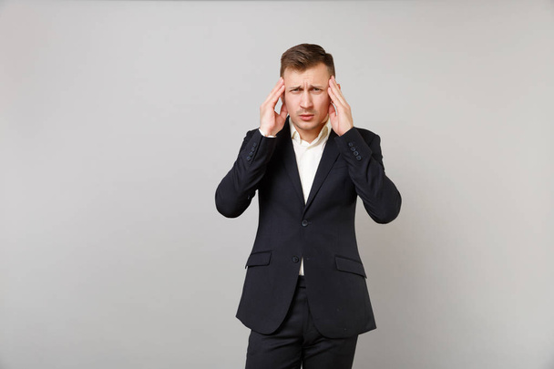 Tired young business man in classic black suit shirt having headache putting hands on head temple isolated on grey background in studio. Achievement career wealth business concept. Mock up copy space - Valokuva, kuva