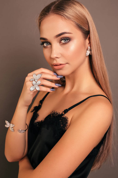 fashion photo of beautiful young girl with blond hair in elegant black dress with jewelry posing in studio - Foto, Imagem