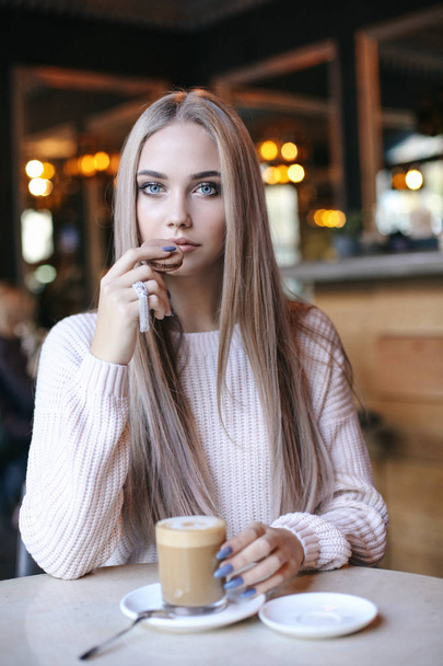 mode foto van mooie jonge vrouw met lang blond haar in elegante kleren zitten in Cafe, een kopje koffie drinken - Foto, afbeelding