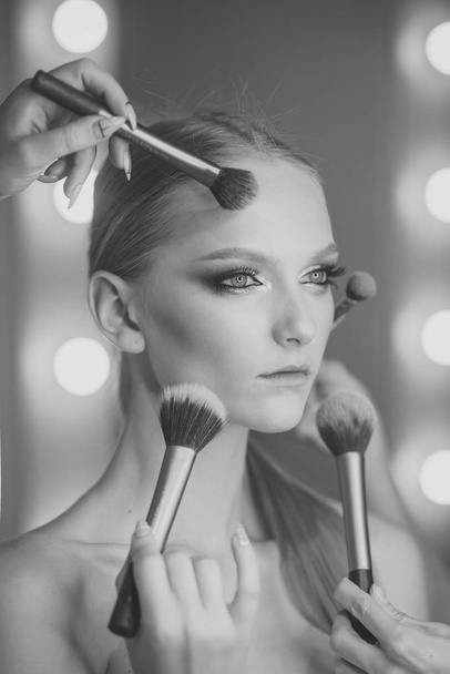 Woman getting powder on skin with makeup brushes. Woman with young face getting makeup in beauty salon - Valokuva, kuva