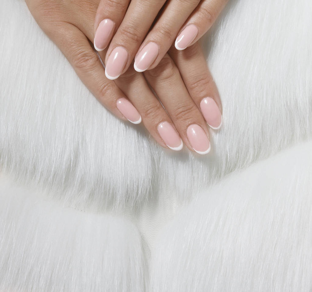 Stylish trendy female pink French manicure on white fur background. - Photo, Image