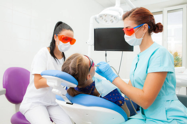 A young woman is a dentist orthodontist and a female assistant treats a patient's teeth lying in a dental chair at a dental clinic. A young woman patient - Fotografie, Obrázek