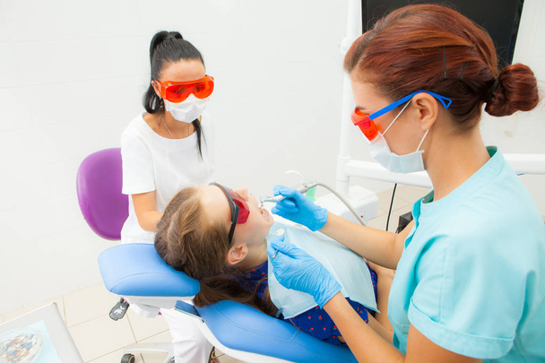 A young woman is a dentist orthodontist and a female assistant treats a patient's teeth lying in a dental chair at a dental clinic. A young woman patient - Valokuva, kuva
