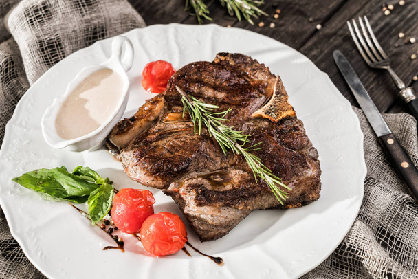 Grilled pork chop steak with rosemary, tomatoes and spices on wooden rustic background. Hot Meat Dishes. Top view, flat lay  - Photo, Image