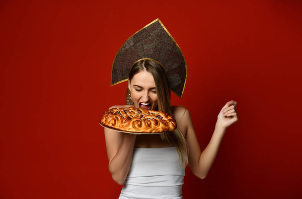 Woman in Russian traditional cap hat kokoshnik happy smiling eat bite sweet cherry homemade pie tasty bun - Valokuva, kuva