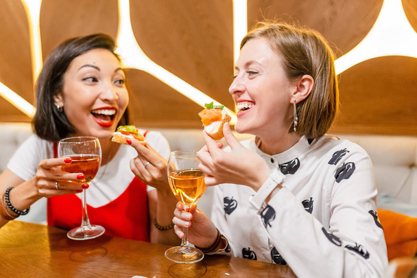 Two female friends Drink wine and enjoy meal at the restaurant - Фото, зображення