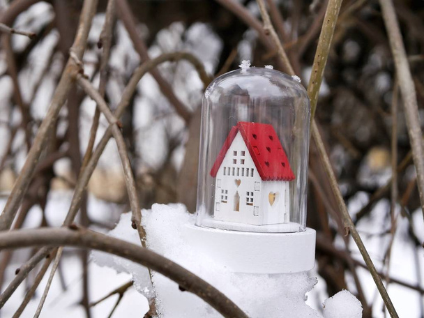  Piccola casa bianca decorativa giocattolo con un tetto rosso e illuminazione illuminata su un albero innevato, il concetto di vacanze invernali stagionali, Natale, una nuova casa nel nuovo anno, comfort domestico
 - Foto, immagini