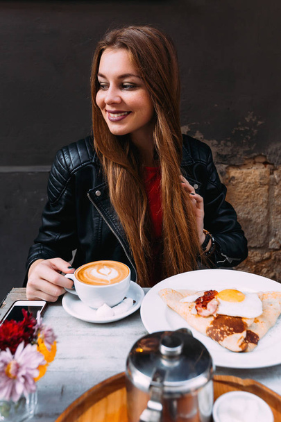 dívka s dlouhými vlasy, sedí u stolu v kavárně. Lahodná snídaně kávy a vejce se slaninou na stůl - Fotografie, Obrázek