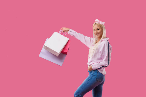 Image of a happy young blonde woman posing with shopping bags over pink background. Shopping concept. Copy space for text - Foto, afbeelding