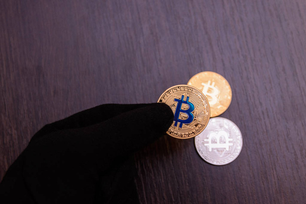  golden bitcoin in man hand in black glove on wooden background - Foto, Bild