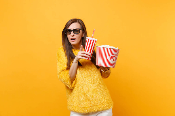 Scared young woman in 3d imax glasses pointing index finger, watching movie film hold bucket of popcorn cup of cola or soda isolated on yellow background. People sincere emotions in cinema, lifestyle - Photo, Image