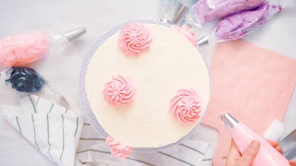 Flat lag. Pastel kleur botterroom rozetten leidingen op een witte cake te maken van een eenhoorn taart. - Foto, afbeelding