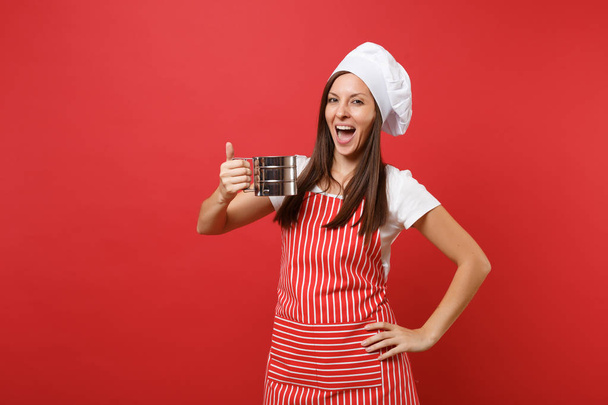 Gospodyni kobiece kobieta kucharz lub piekarz w paski fartuch kuchenny, biały t-shirt, toczek kucharzy kapelusz na białym tle na tle czerwone ściany. Gospodyni kobieta trzymać żelazo metalowe sito przesiewania mąki. Makiety koncepcja przestrzeni kopii - Zdjęcie, obraz
