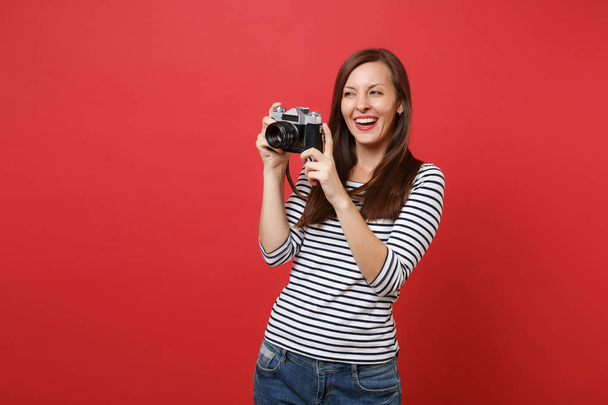 Portret van lachende mooie jonge vrouw in gestreepte kleren retro vintage fotocamera geïsoleerd op heldere rode muur achtergrond te houden. Mensen oprechte emoties, lifestyle concept. Bespotten kopie databaseruimte - Foto, afbeelding