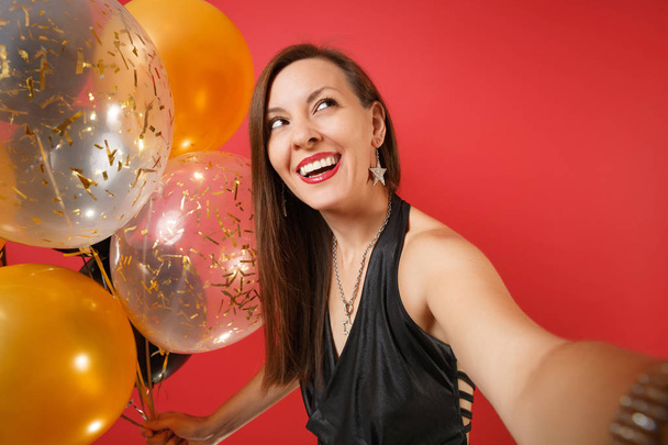 Primer plano de foto selfie de niña sonriente en vestido negro celebrando la celebración de globos aéreos aislados sobre fondo rojo brillante. Día de San Valentín Feliz Año Nuevo, concepto de fiesta de cumpleaños mockup fiesta
 - Foto, Imagen
