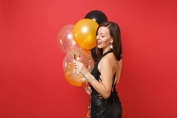 Side view of attractive woman in black dress celebrating holding glass of champagne, air balloons isolated on red background. St. Valentine's Day, Happy New Year birthday mockup holiday party concept - Photo, Image