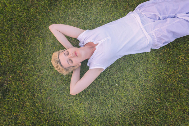 vista superior da mulher jovem relaxando na grama enquanto deitado com as mãos atrás da cabeça, relaxamento e conceito de natureza
 - Foto, Imagem