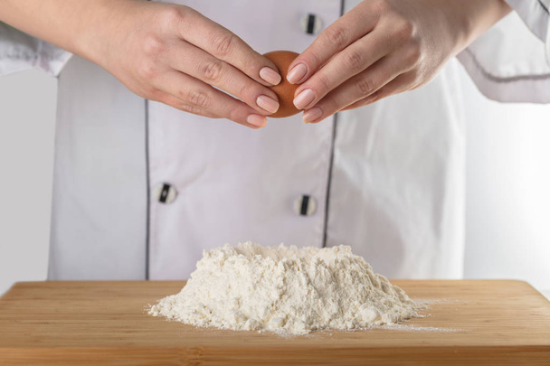 Cook adds an egg into the flour - Φωτογραφία, εικόνα