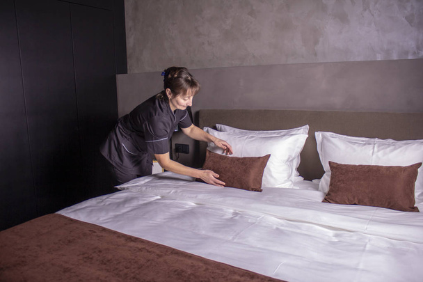 Hotel maid setting up pillow on bed sheet in hotel room - Photo, Image
