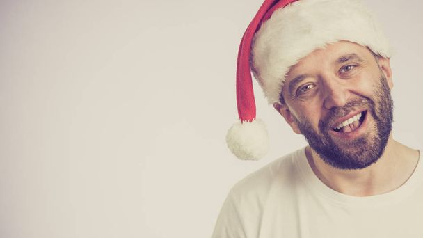 Bearded man wearing santa claus hat portrait, on grey with copy space. Christmes time. - Photo, Image