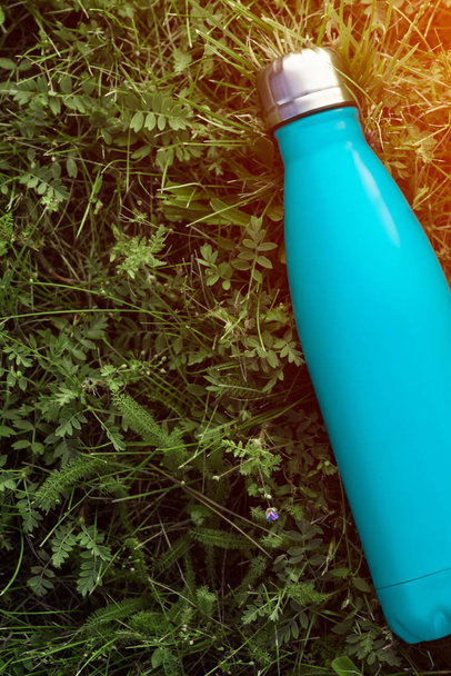 Edelstahl Thermoskanne, matte hellblaue Farbe. Attrappe isoliert auf grünem Gras Hintergrund mit Sonnenlicht-Effekt - Foto, Bild