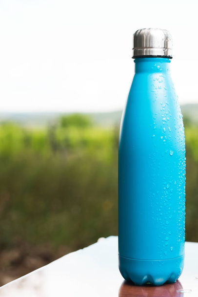 Stainless thermos bottle for water on table outdoor. Light blue color - Photo, Image