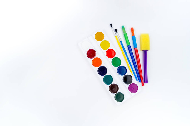 Watercolor paints and brush on a white background. Copy space. Flat lay. Back to school. Tools for the student. Colors of rainbow - Photo, Image