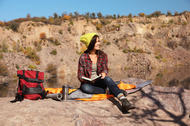 Female camper reading book while sitting on sleeping bag in wilderness - Foto, Imagem