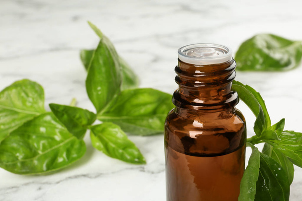 Bottle of basil essential oil and fresh leaves on marble table, closeup. Space for text - Photo, Image