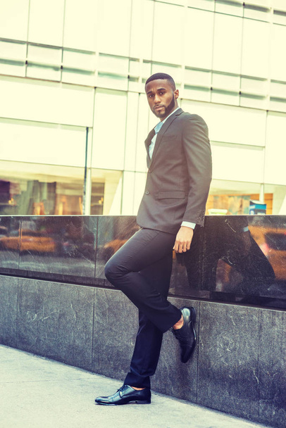Nuoren afroamerikkalaisen liikemiehen muotokuva. Nuori musta mies, jolla on parta New Yorkissa, yllään musta takki, housut, nahkakenkä, seisoo kadulla Manhattanin Middletownissa, innolla
. - Valokuva, kuva