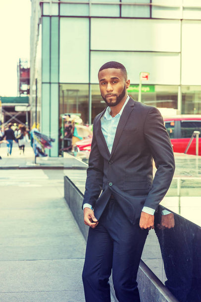 Joven hombre afroamericano guapo con barba viajando por Nueva York, vistiendo chaqueta negra, pantalones, camiseta blanca, parado en la calle en Middletown de Manhattan, mirando a su alrededor
 - Foto, imagen