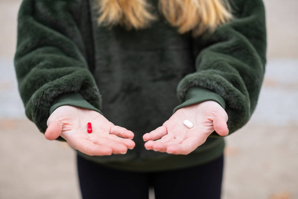 Unerkennbare junge Frau zeigt zwei verschiedene Medikamententabletten in Händen, während sie im Park steht - Foto, Bild