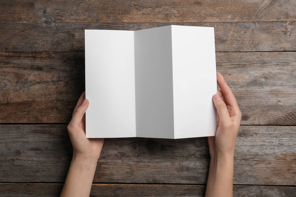 Woman with blank brochure on wooden background, above view. Mock up for design - Foto, afbeelding