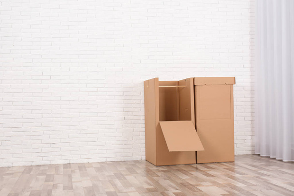 Empty cardboard wardrobe boxes against brick wall indoors. Space for text - Photo, Image