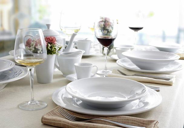 Table de restaurant avec plats blancs, couverts et verres à vin
  - Photo, image