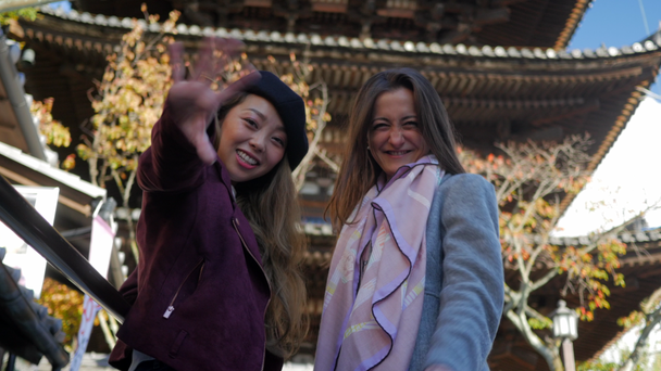 4k ενθουσιασμένος γυναίκας κουνώντας και χαμογελά στη φωτογραφική μηχανή, μεγάλος ναός Κιότο πίσω, χαμηλή γωνία. - Πλάνα, βίντεο