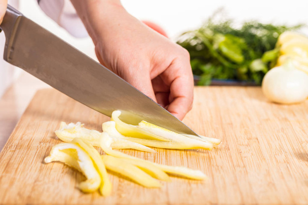 Cook cuts pepper with a knife on wooden board - Fotoğraf, Görsel
