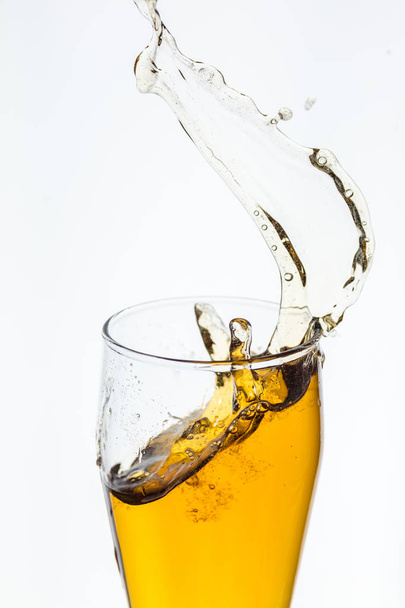 Splashing beer from a glass on white background - Foto, Imagen