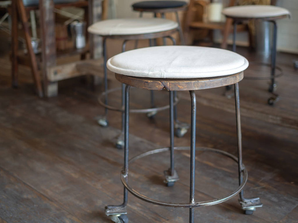 Old vintage iron and wooden bar stools with wheels with black and white fabric pad on top on wooden floor in cafe decoration retro style. - Foto, afbeelding