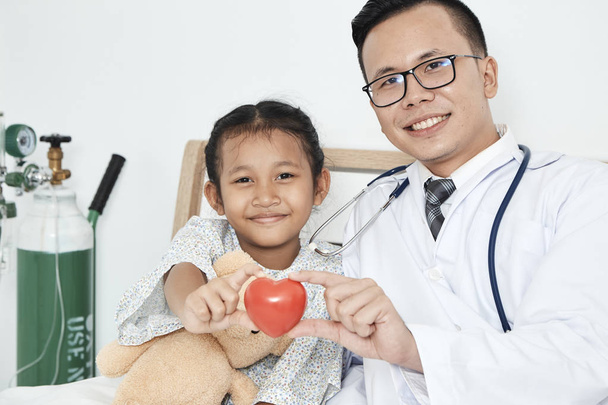Догляд, Доктор зі стетоскопом, який тримає червоне серце та дівчинку в кімнаті пацієнта, Концепція охорони здоров'я та медицини - обізнаність про дівчину з раком
 - Фото, зображення