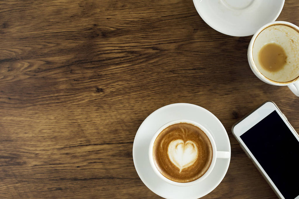 Filiżanka kawy z serca wzór w białe filiżanka i inteligentny telefon na podłoże drewniane, widok z góry, pomysły dla prowadzenia biznesu w Internecie - Zdjęcie, obraz