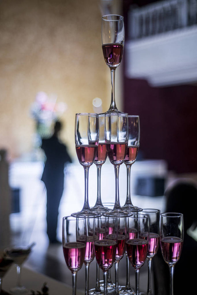 A beautiful table setting with empty or full glasses of wine or champagne that stand on top of each other as a slide or triangle on a dark background in the interior of a cafe and restaurant. - Photo, image