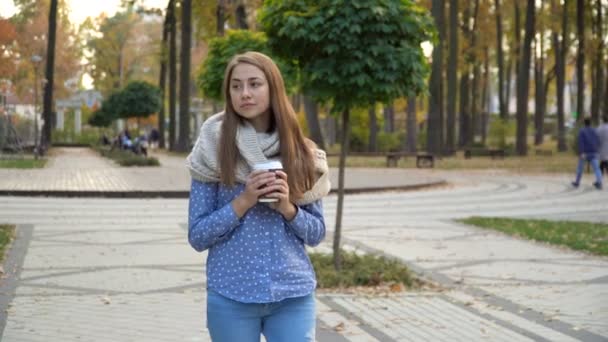 Primo piano del volto della donna che beve tè caldo o caffè nel parco autunnale, indossa sciarpa lavorata a maglia. ragazza beve caffè per buon umore da tazza
. - Filmati, video