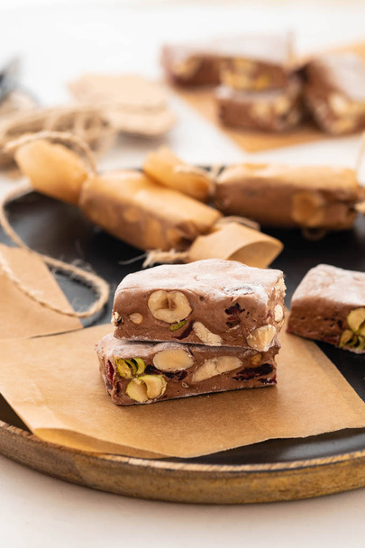 A variety of different nutty nougat in dark chocolate with roasted hazelnuts cut open to show the nougat mix on a wooden board . Copy space. - Foto, immagini