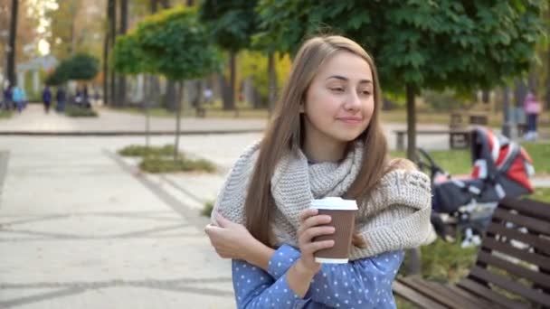 Close-up van het gezicht van een vrouw die hete thee of koffie in herfst park drinkt, ze draagt gebreide sjaal. meisje drinkt koffie voor goed humeur uit mok. - Video