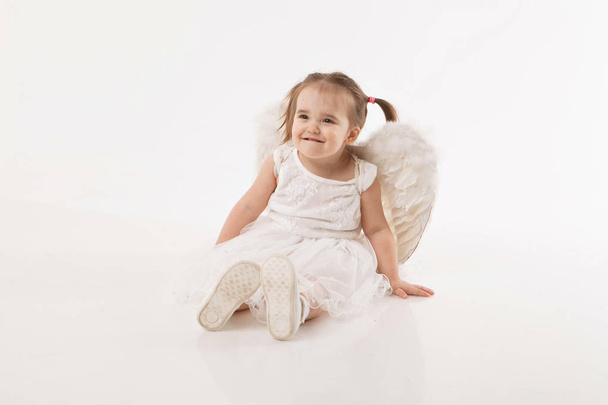 little girl in white dress with wings playing on white background - Fotoğraf, Görsel