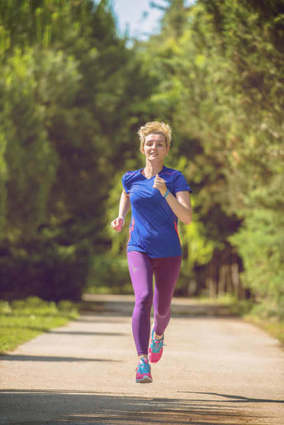 若いスポーティな女性ランナーの晴れた朝の美しい熱帯公園でマラソンのトレーニング - 写真・画像