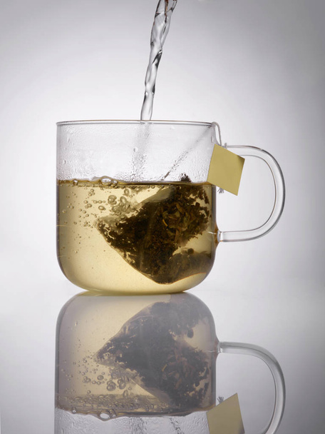 Nahaufnahme von Glas-Teetasse mit Teepaket auf grauem Hintergrund  - Foto, Bild
