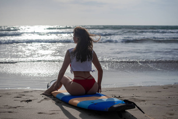 Beach lifestyle people - woman enjoying summer sun and blue sky sitting relaxing with surfboard after bodyboarding in water. Beautiful multiracial Asian Caucasian female bikini girl on travel vacation - Valokuva, kuva